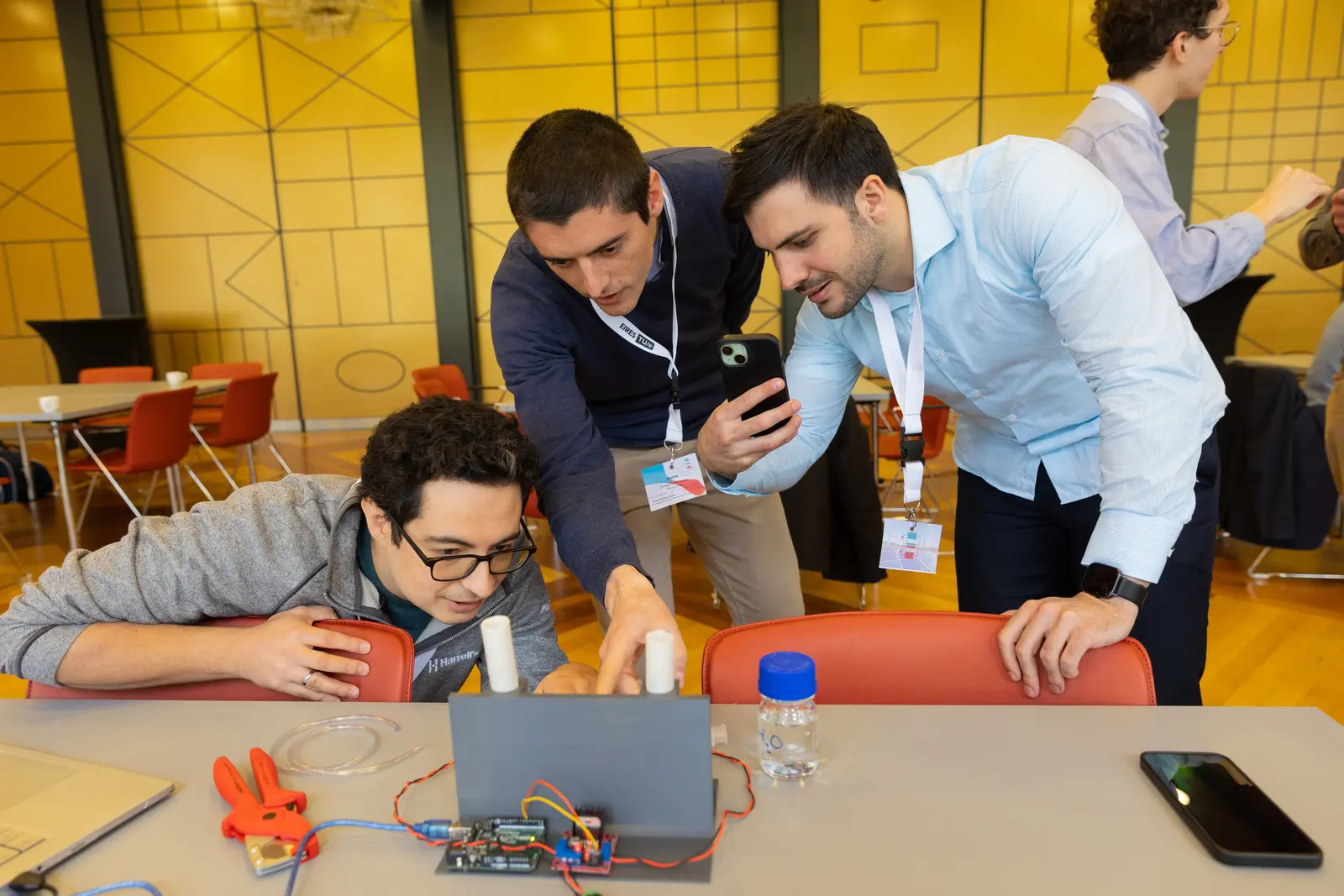 Three people watching a leak test in the flow cell jig on a table in a conference room, all looking closely at the setup